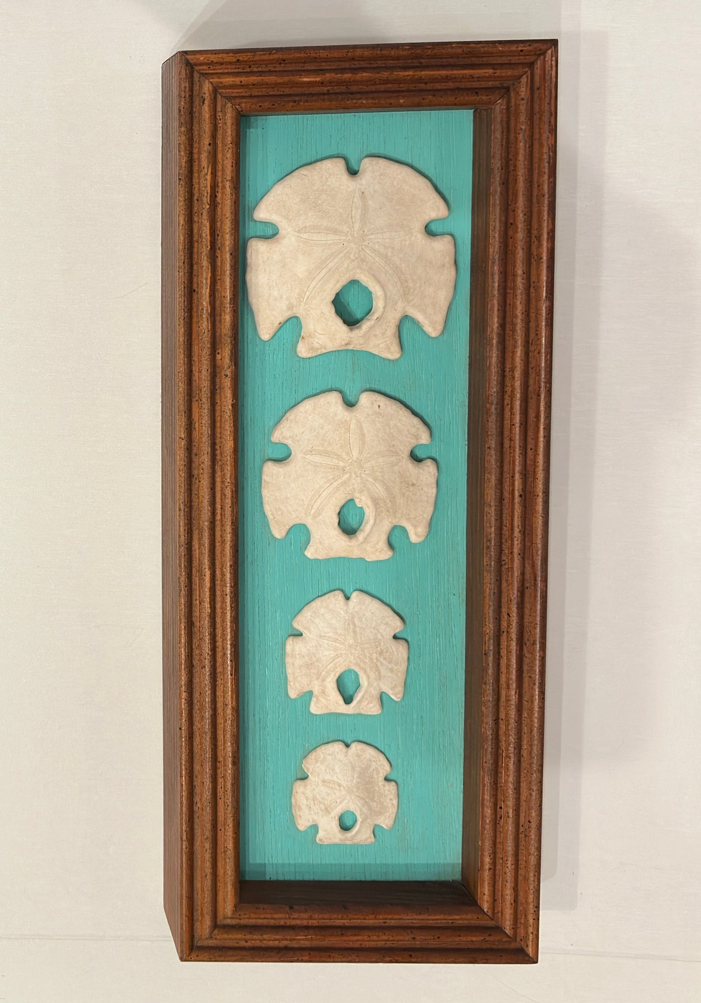 Decorative wall art with three shell-like sculptures on a turquoise background, framed in wood.