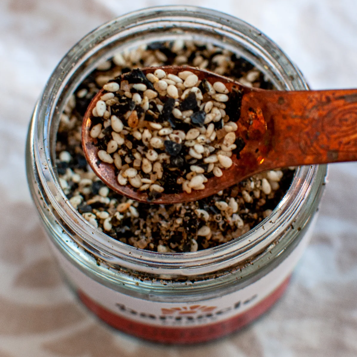 Jar of mixed seeds with a wooden spoon on a textured surface