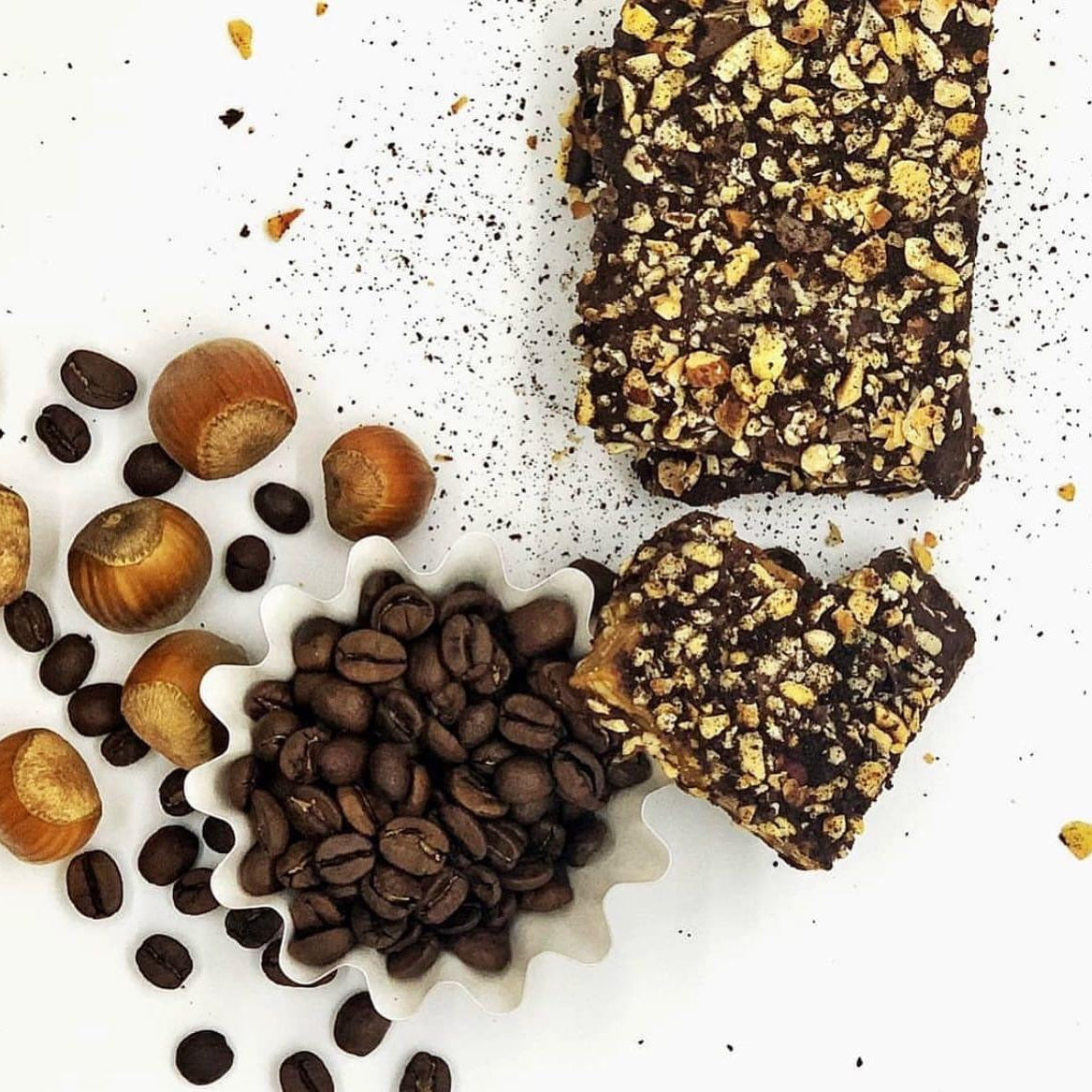 Toffee bars covered with dark chocolate and hazelnuts, alongside Oregon-grown hazelnuts and coffee beans.