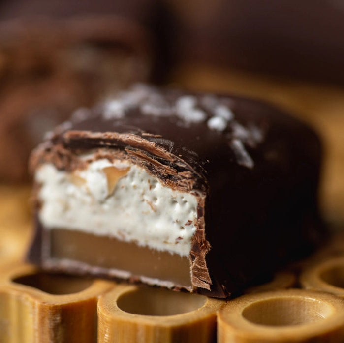Cut in half candy with chocolate covering a layer of caramel topped with fluffy white nougat
