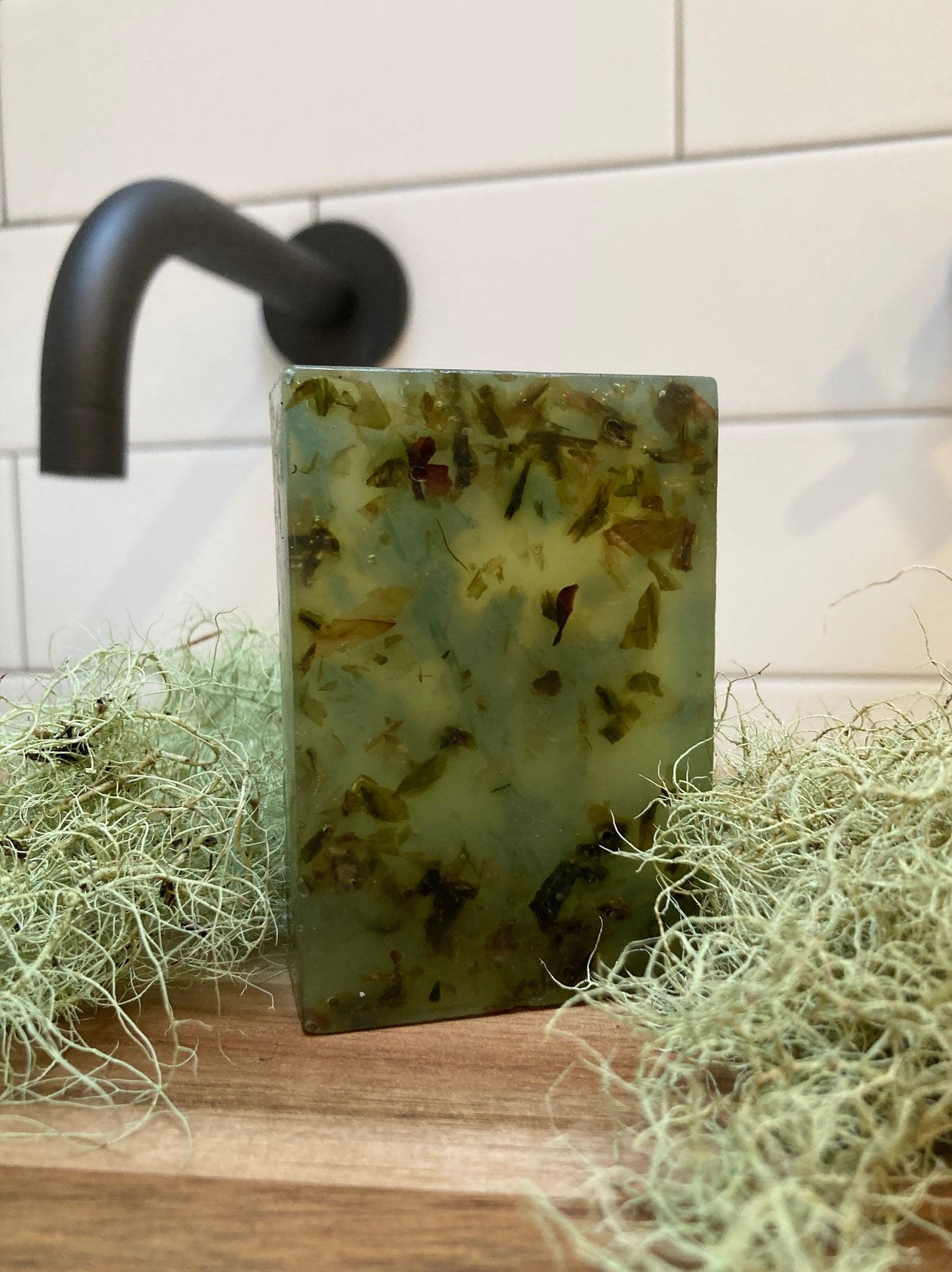 An unwrapped bar of the seaweed soap on a wooden table with a white tile behind it and black sink faucet coming out of the wall.