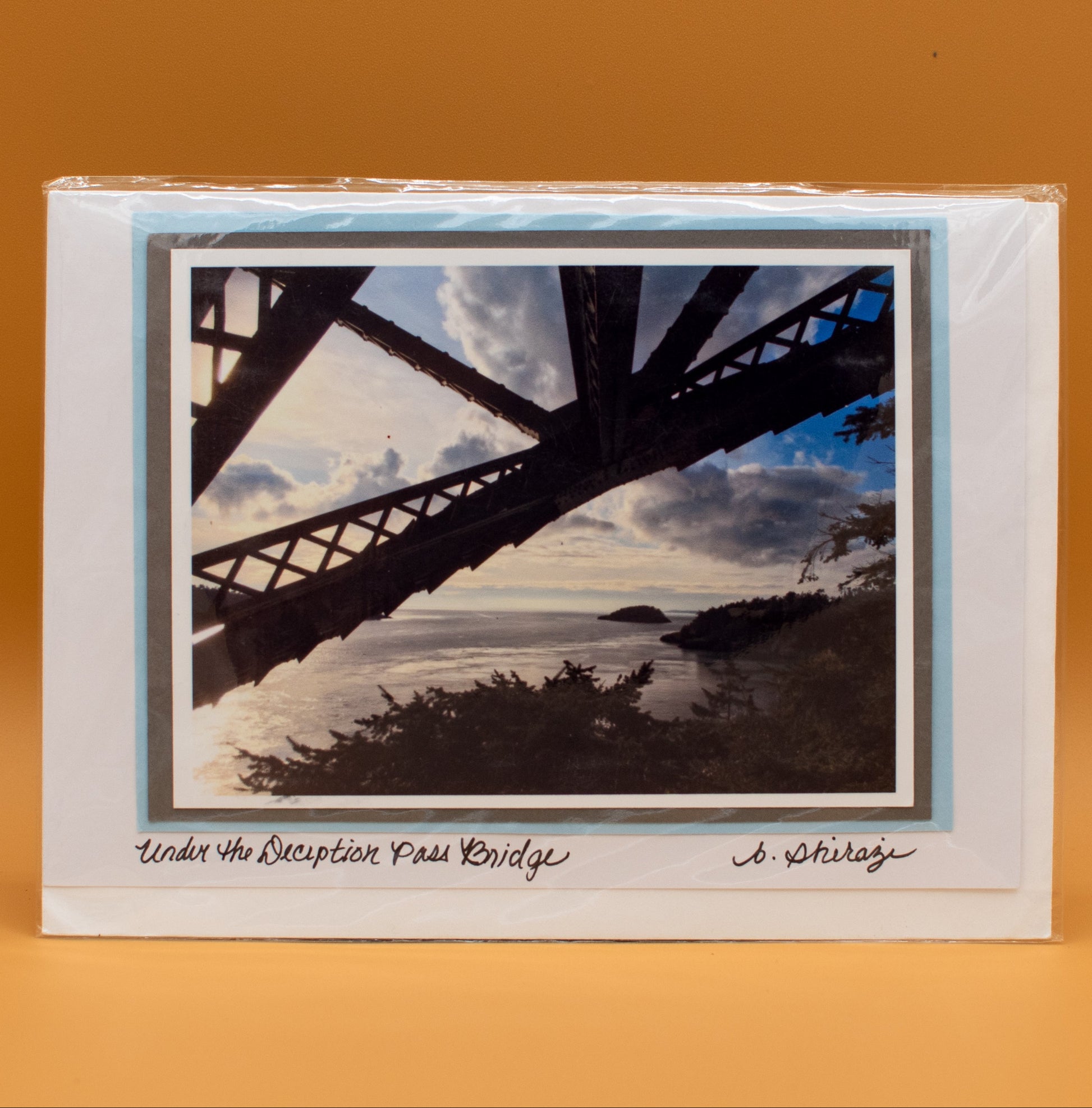 Photo of Deception Pass Bridge, attached to a white greeting card with the handwritten words "Under the Deception Pass Bridge, B Shirazi"