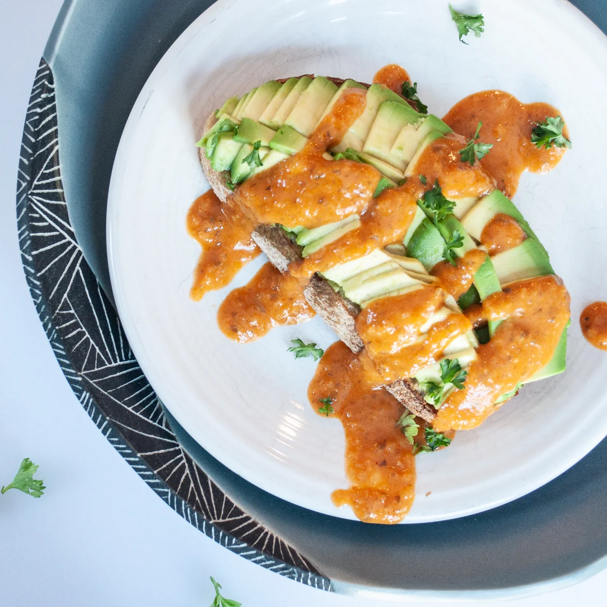 Plated dish with avocado toast covered in red-orange hot sauce on a white plate with a blue rim.