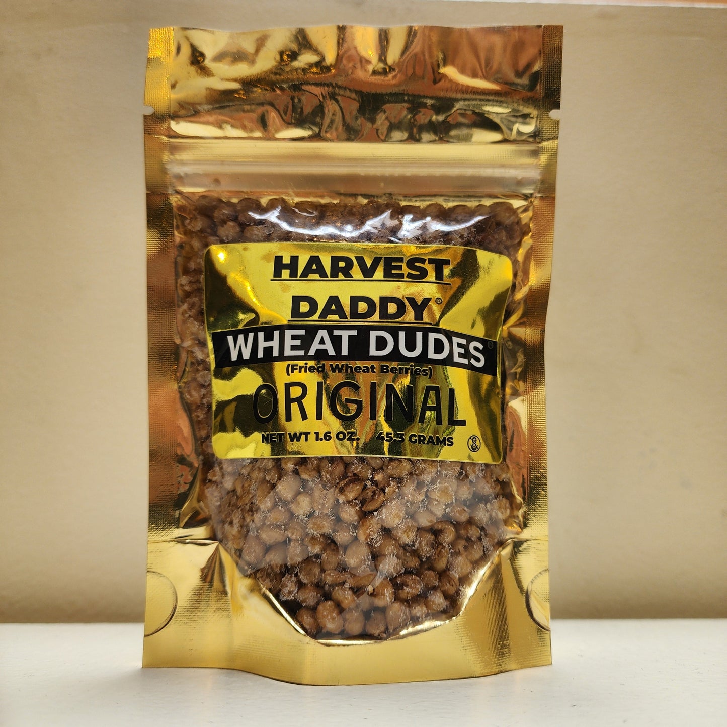 A bag of Harvest Daddys Original Wheat Dudes (fried wheat berries), shown in a gold metallic stand-up pouch with a clear window displaying brown wheat kernels inside.