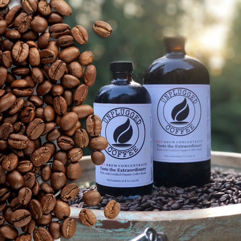 Coffee beans spilled on a photo of two glass bottles  that say UNPLUGGED COFFEE HOT BREW CONCENTRATE. 