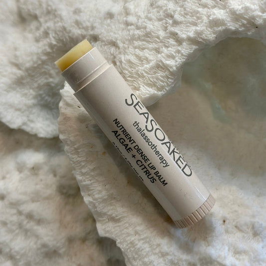 A white tube of lip balm on a textured white shell background. The tube sas "SeaSoaked thalassotherapy NUTRIENT DENSE LIP BALM ALGAE + CITRUS"