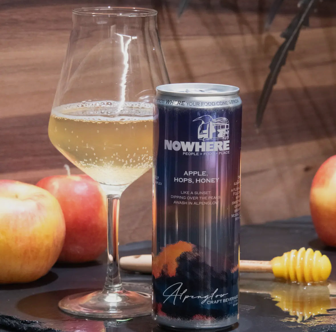 A can of Alpenglow sparkling mocktail with a image of a glass filled with the drink, alongside whole apples and a honey dipper.