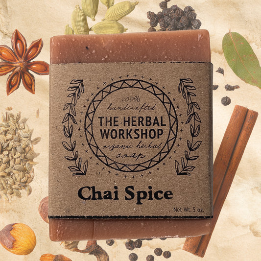 Bar of soap from The Herbal Workshop with 'Chai Spice' flavor on a background of spices and herbs.