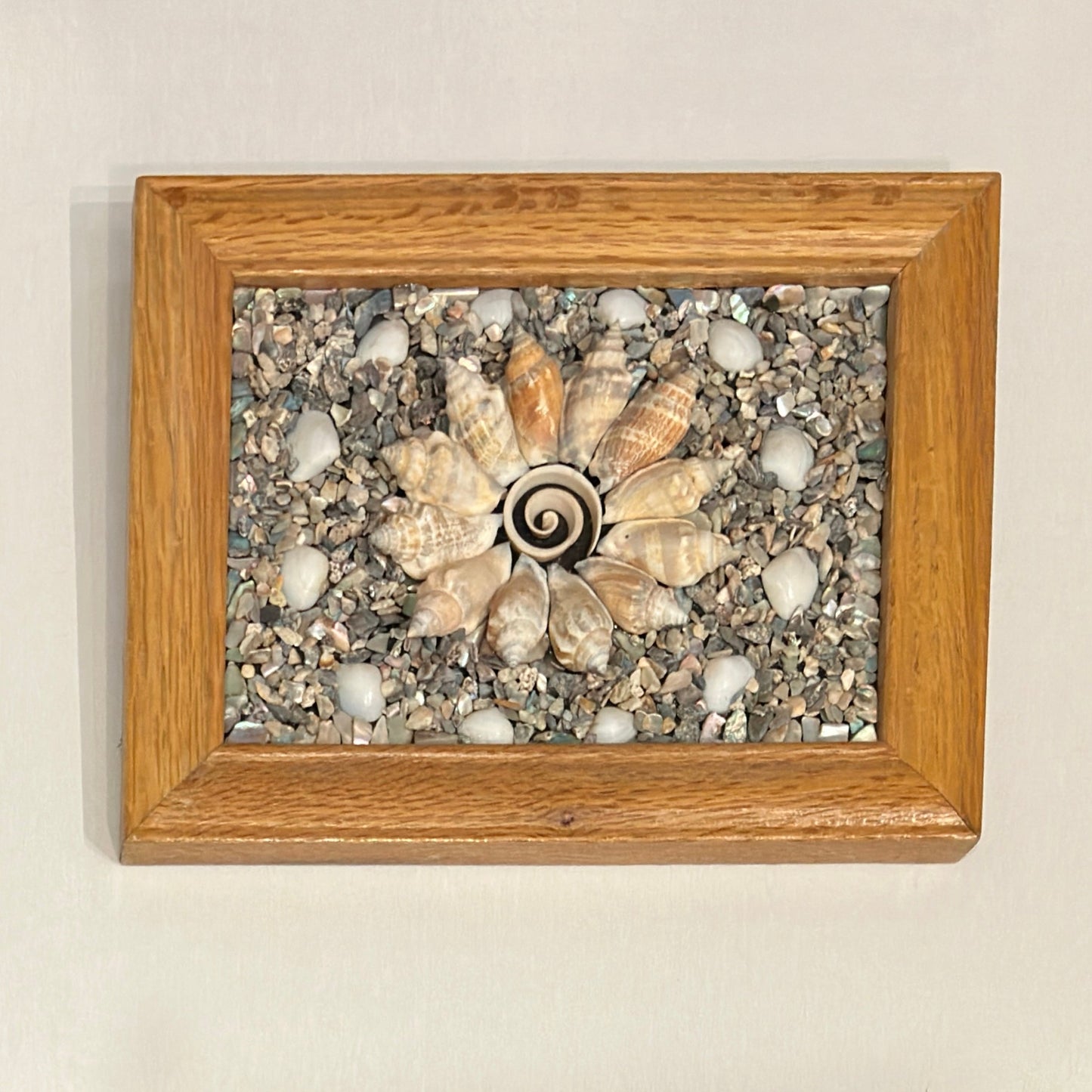 Decorative wall art with shell and stone design in a wooden frame on a beige wall.