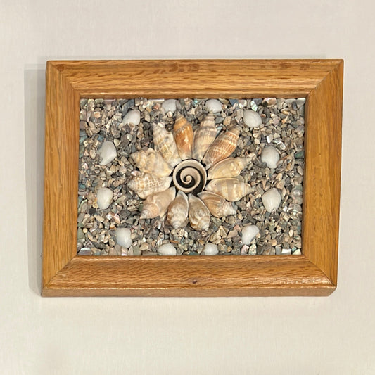 Decorative wall art with shell and stone design in a wooden frame on a beige wall.