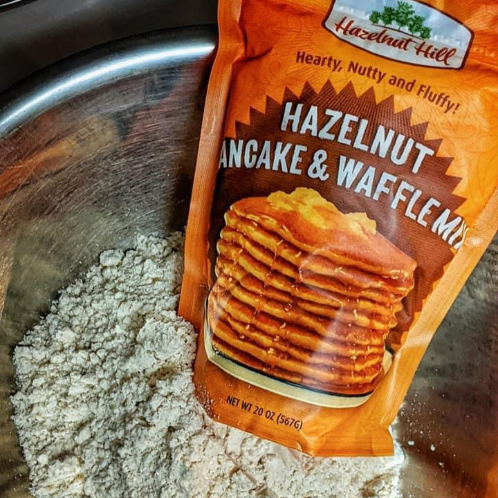 Packaged Hazelnut Hill Pancake & Waffle Mix on a metal surface with flour.