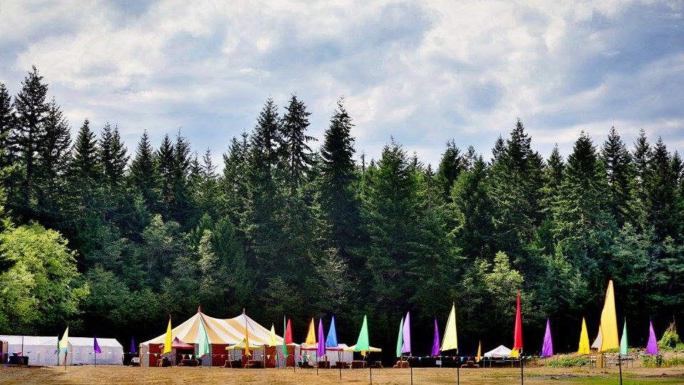Orange and white striped circus tent and colorful flags set up in a field with trees in the background