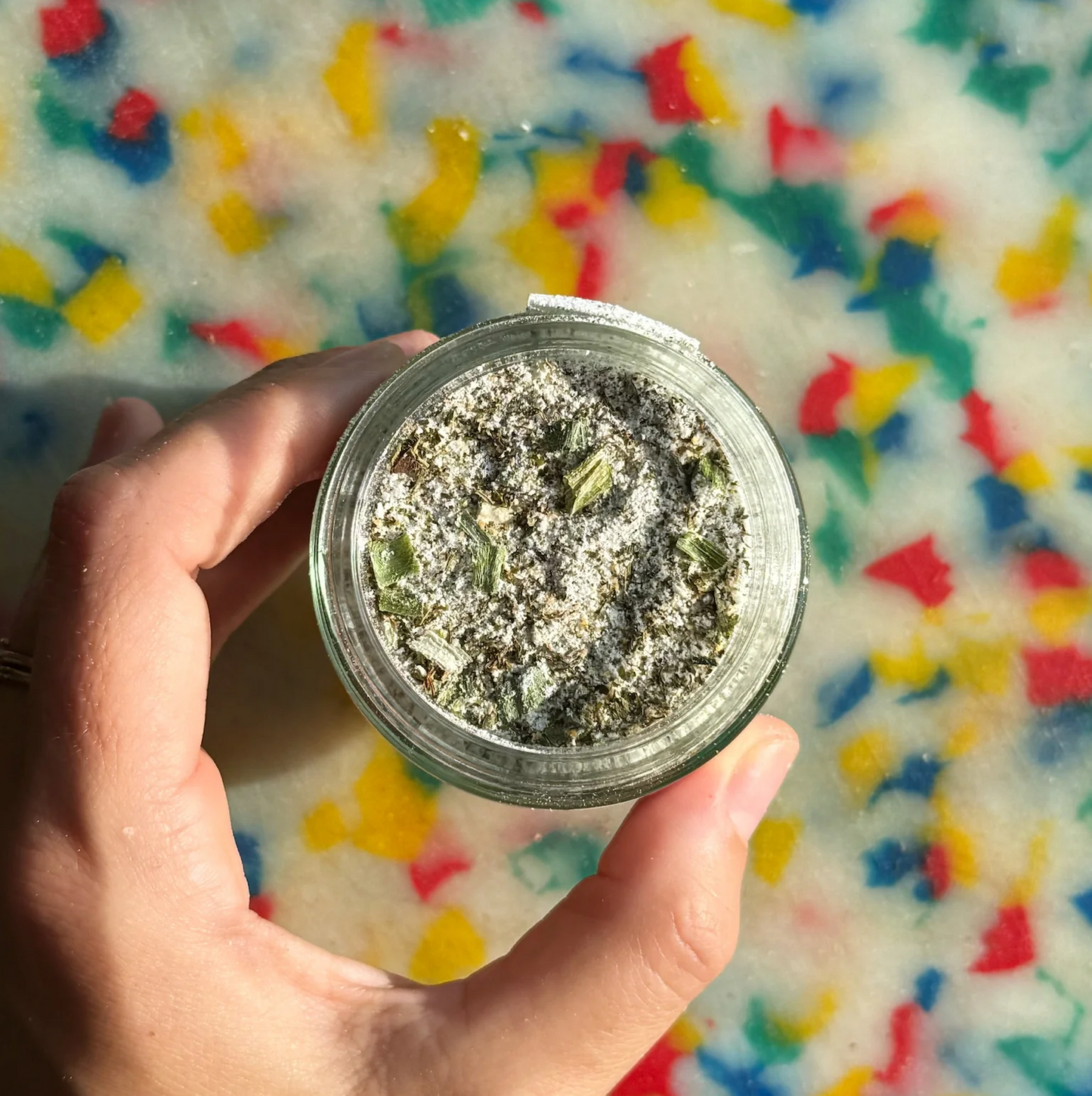 Hand holding a jar of dried herbs with a colorful, abstract background