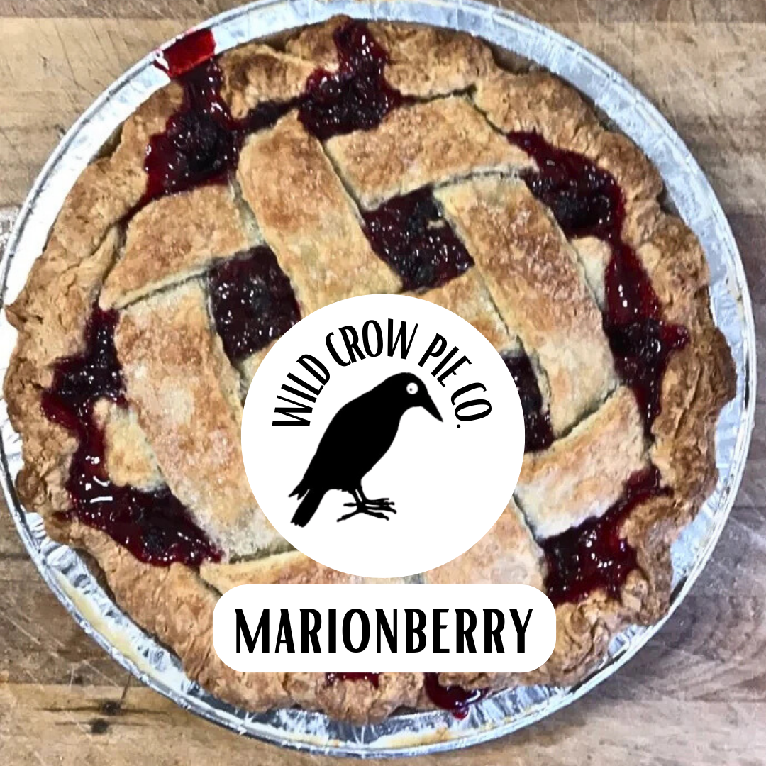 Marionberry pie on wooden background, with the Wild Crow Pie Co. logo on a white circle