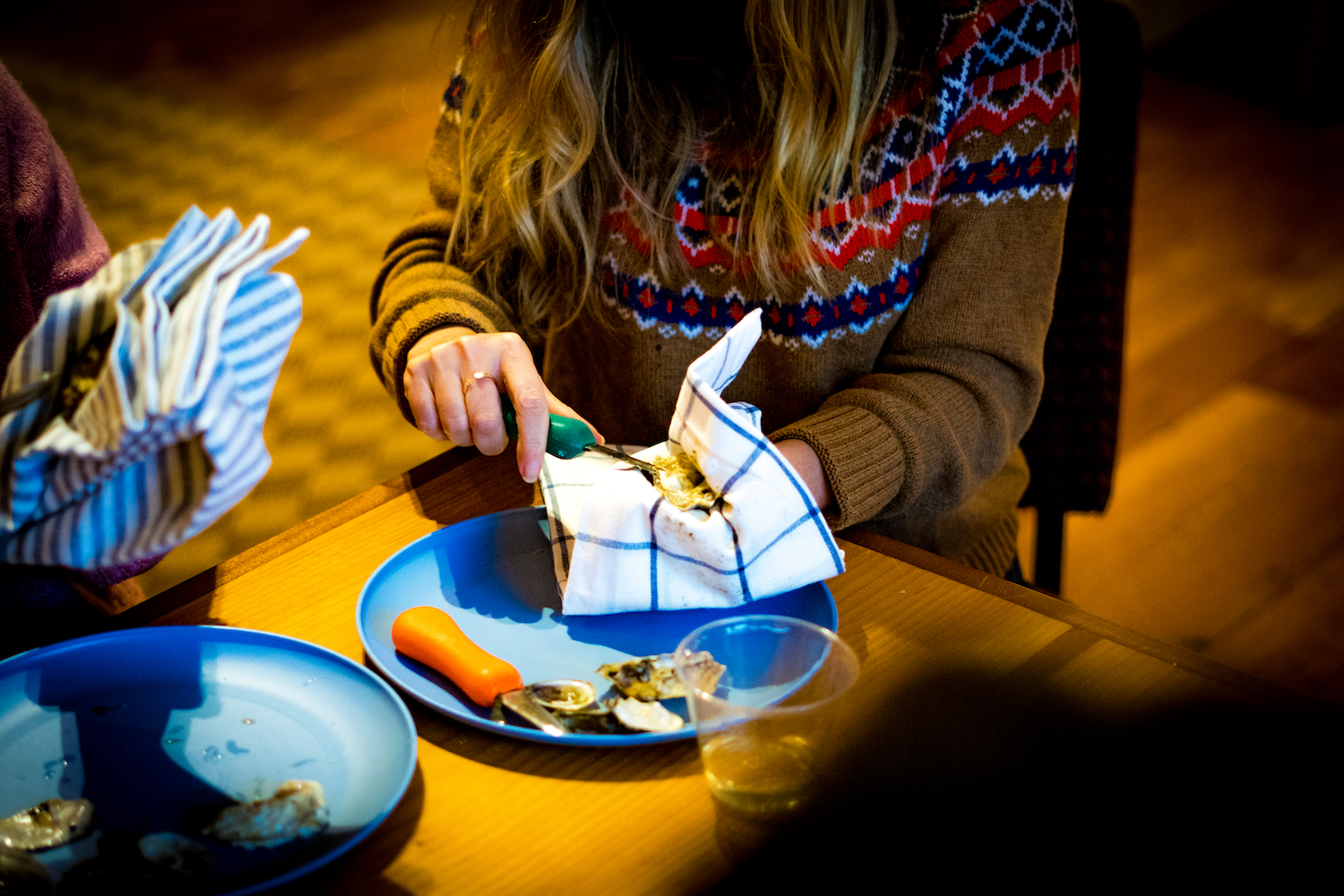 Person sitting at a table with a plate of food and cutlery, wearing a patterned sweater.