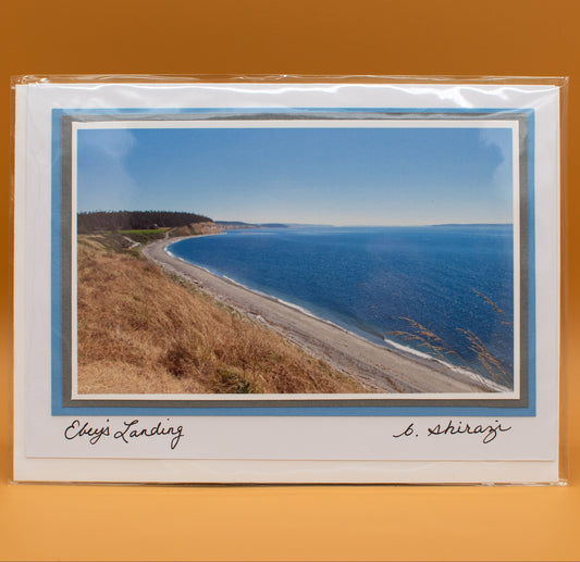 Photo of the Puget Sound water and beach seen from a high bluff with golden dried wild grass, attached to a white greeting card with the handwritten words "Ebey's Landing, B Shirazi"