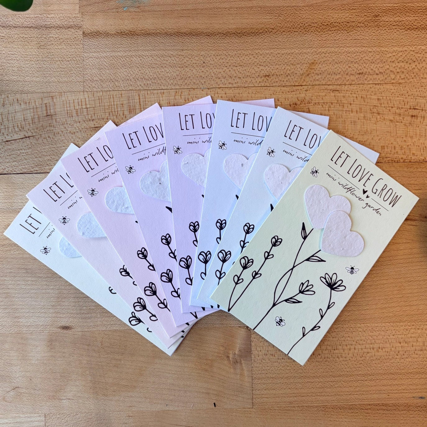 Set of seed paper cards with 'Let Love Grow' text on a wooden surface.
