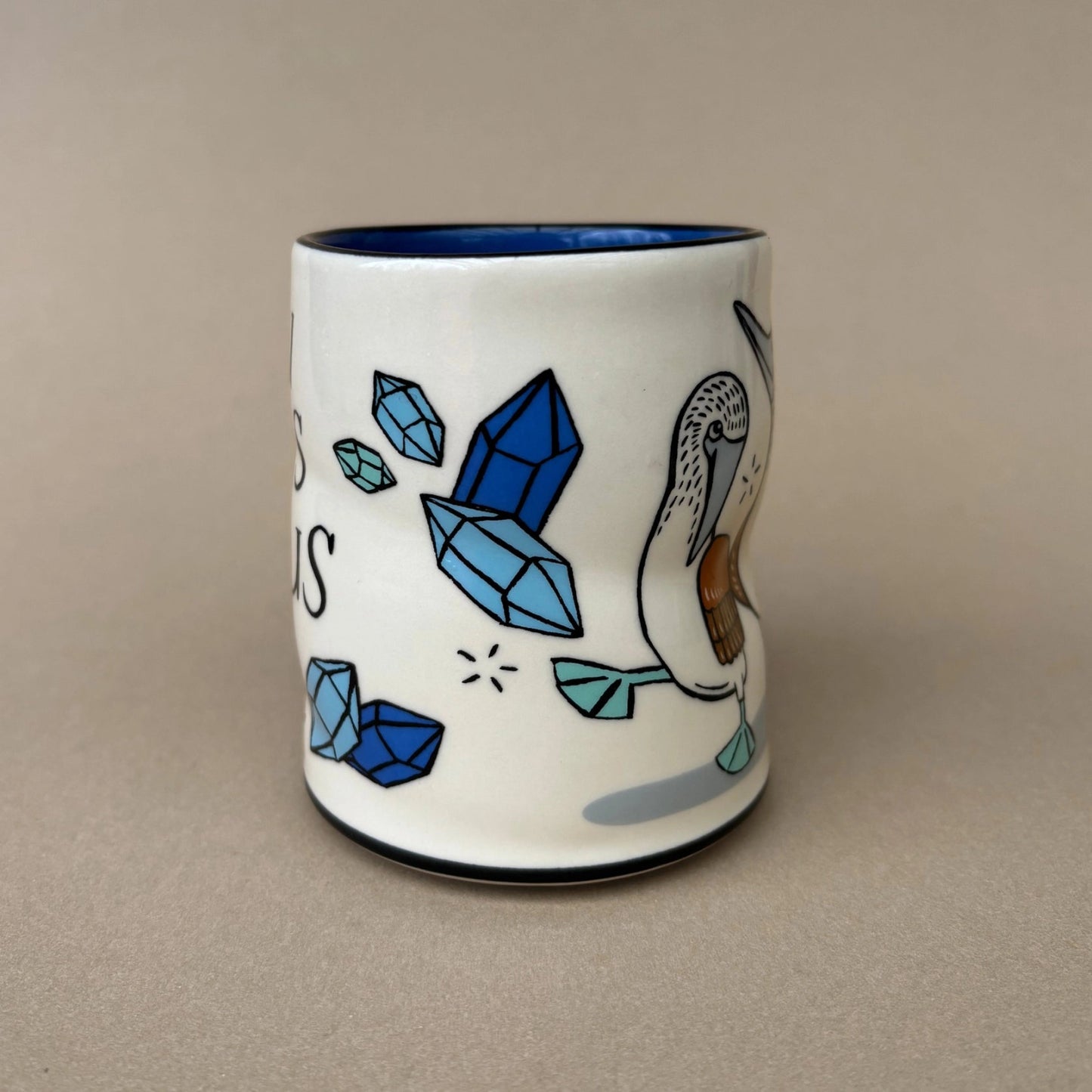 Ceramic mug with blue crystals and a pelican design on a beige background