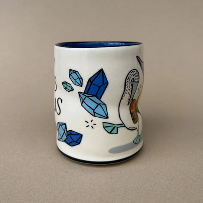 Ceramic mug with blue crystals and a pelican design on a beige background