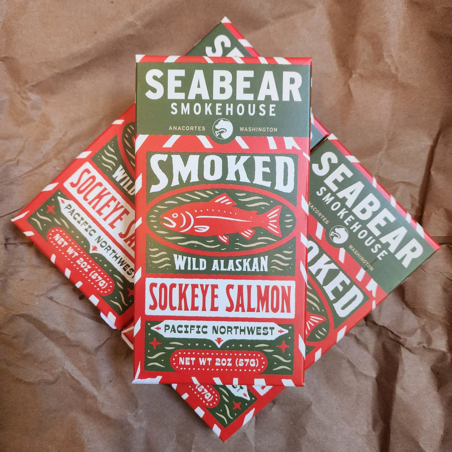 Four boxes of Seabear Smokehouse Sockeye Salmon smoked meat arranged on a brown paper background. The packaging features a bold red, green, and white design with a stylized sockeye salmon illustration.