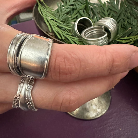 A selection of metal rings made from spoons, displayed on a person's fingers, with the rings showing various designs and finishes.