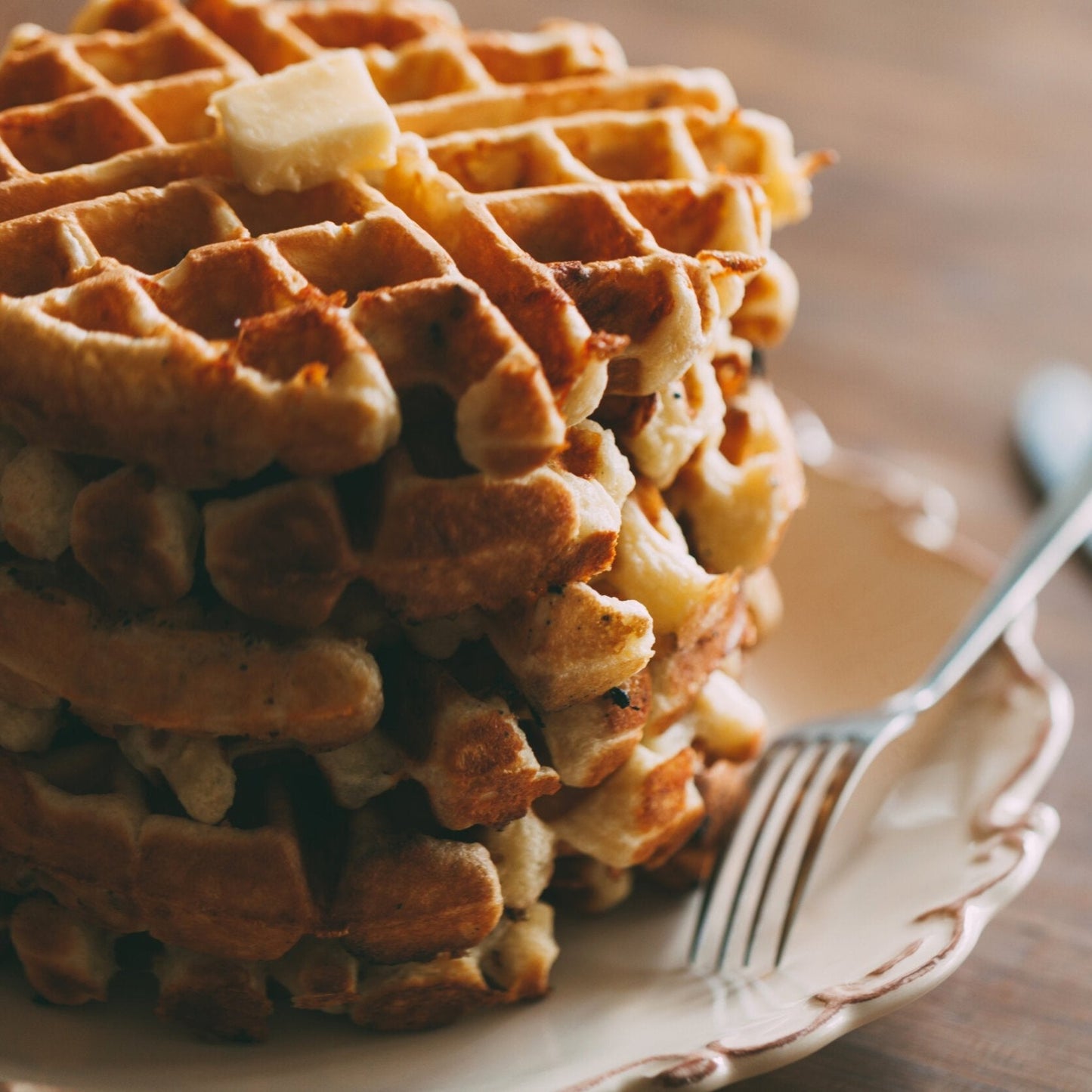 Stack of waffles on a plate with a fork and knife on a wooden table