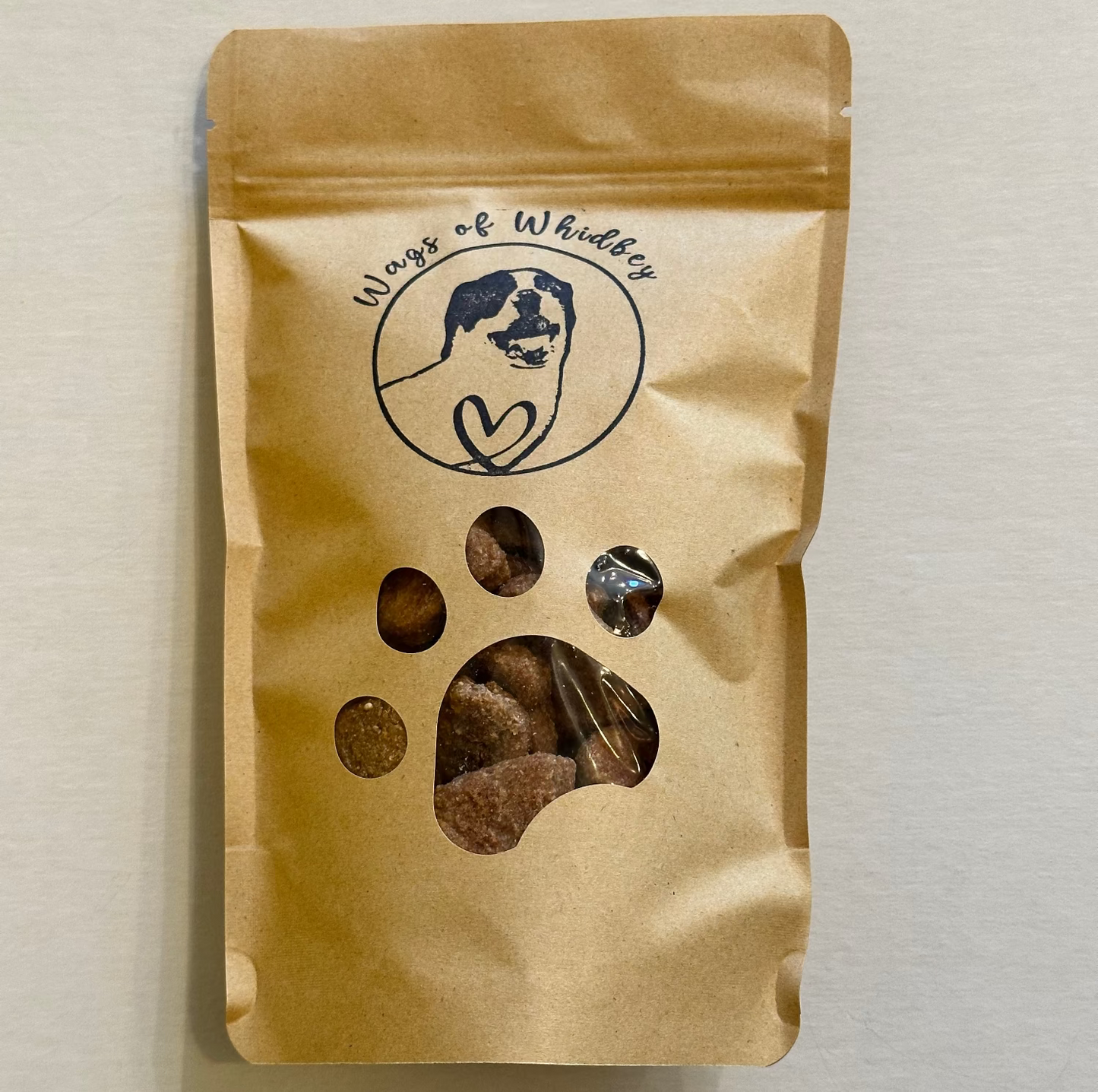 Kraft paper packaging with a paw print cut-out showing the treats inside, and a stamp of a dog with the words 'Wags of Whidbey'