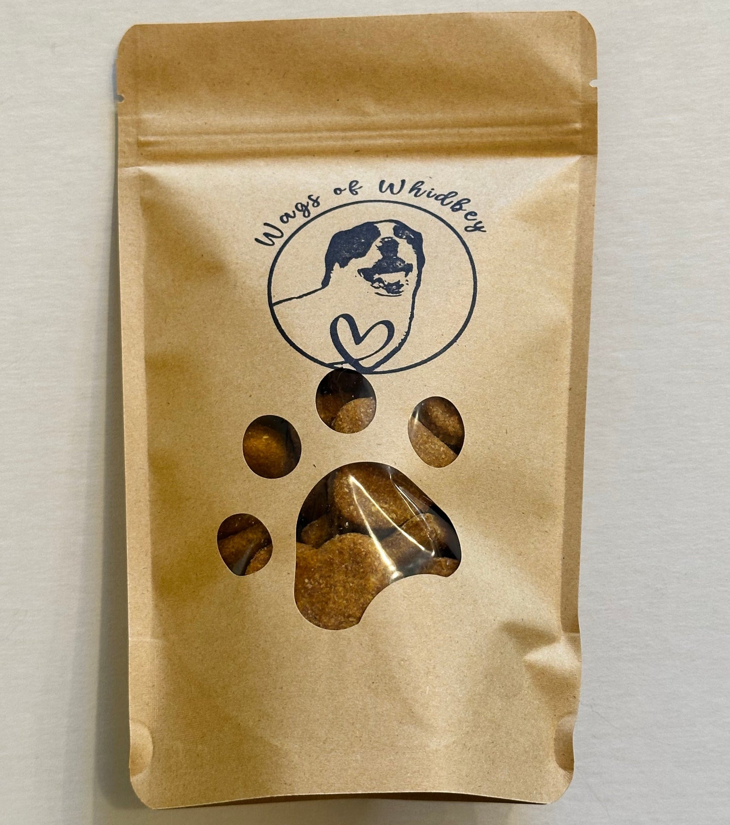 Kraft paper packaging with a paw print cut-out showing the treats inside, and a stamp of a dog with the words 'Wags of Whidbey'